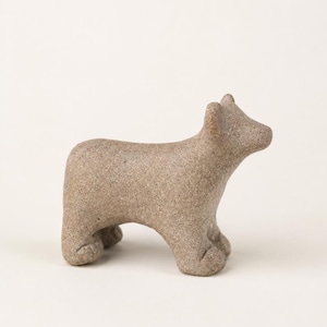 May include: A small, standing animal figurine crafted from a textured, light brown stone-like material. The sculpture features a simplified, rounded form with four sturdy legs, a short tail, and pointed ears, capturing a quadrupedal creature.