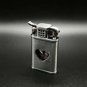 May include: A silver lighter with a heart-shaped cutout on the front. The lighter has a brass wick and a black wick cover.