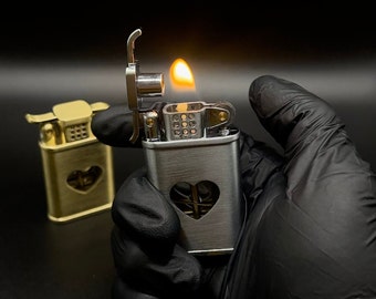May include: A silver lighter with a heart-shaped cutout and a flame coming out of the top. The lighter is being held in a black gloved hand.