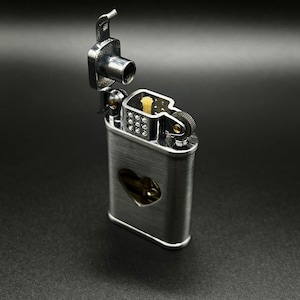 May include: A silver lighter with a heart-shaped cutout on the front. The lighter is open, revealing the flint and wick.