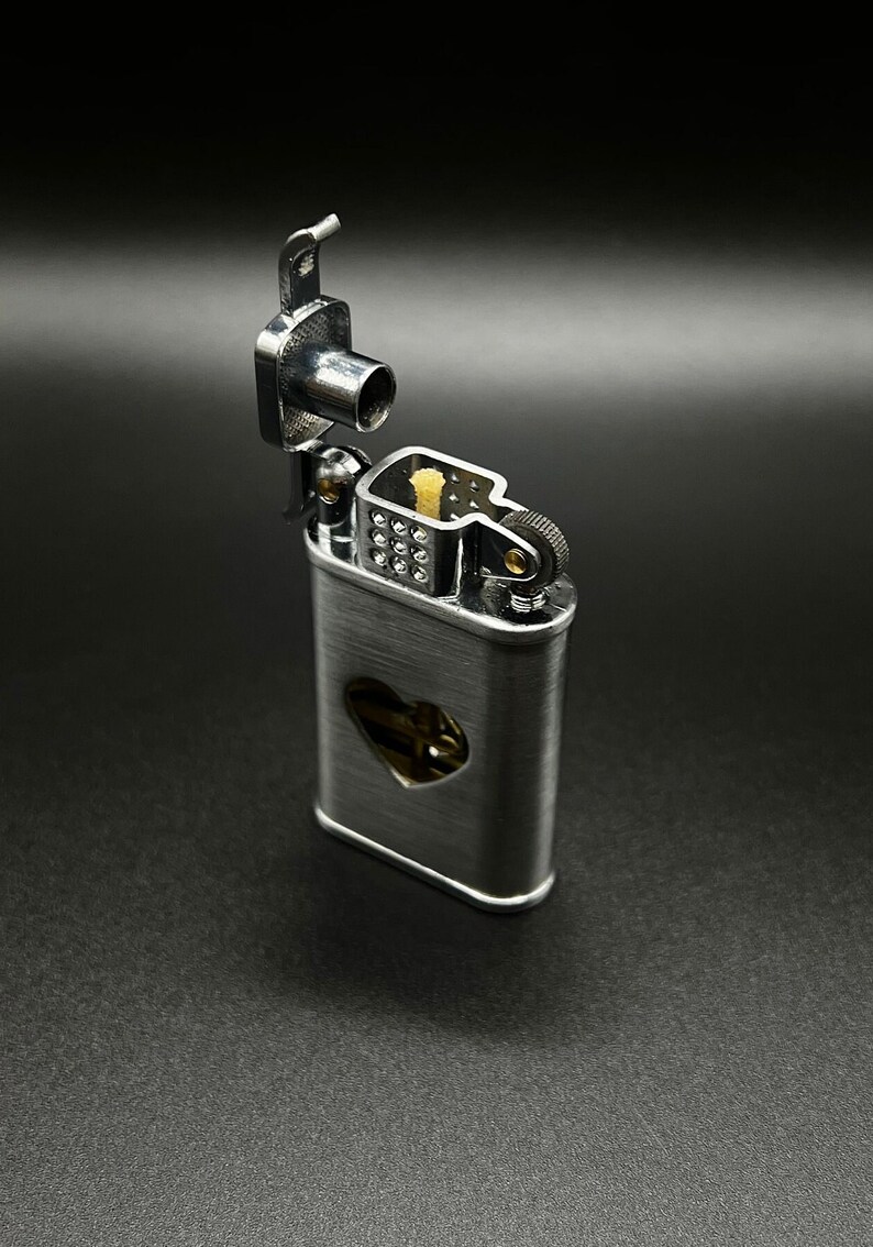 May include: A silver lighter with a heart-shaped cutout on the front. The lighter is open, revealing the flint and wick.