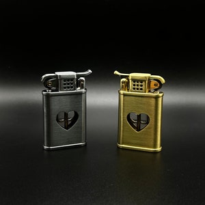 May include: Two lighters with a heart-shaped cutout design. One lighter is silver and the other is gold.