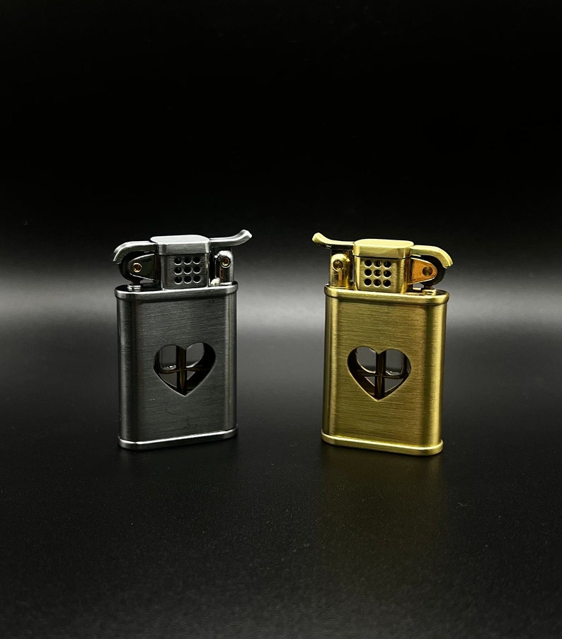 May include: Two lighters with a heart-shaped cutout design. One lighter is silver and the other is gold.