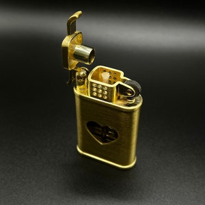 May include: A gold-colored lighter with a heart-shaped cutout on the front. The lighter is open, revealing the wick and flint.