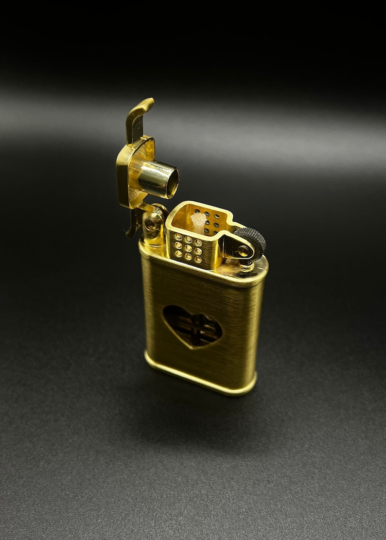 May include: A gold-colored lighter with a heart-shaped cutout on the front. The lighter is open, revealing the wick and flint.