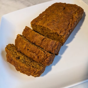 May include: A loaf of pumpkin bread sliced on a white plate. The bread is a light brown color and has a slightly crumbly texture.
