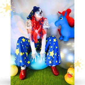 May include: A clown costume featuring blue trousers with yellow stars, a white top with daisy patterns, and a blue hat with yellow stars. The outfit includes long white gloves, red clogs, and a wig with long red and blue braids. The clown has white face paint.