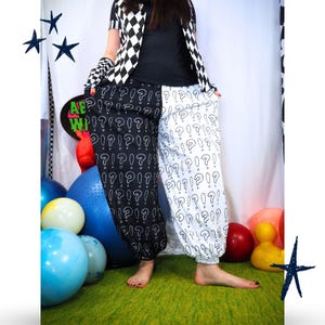 May include: Loose-fitting pants featuring a split design with a black left leg and a white right leg, both covered in a repeating pattern of white and black question marks. The pants have an elasticized waistband and cuffed ankles.
