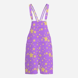 May include: Purple short dungarees featuring a repeating pattern of yellow stars in various sizes. The garment includes adjustable shoulder straps with metal buckles and a front bib pocket, showcasing a consistent star print across the entire surface.