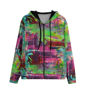 Op de afbeelding: Een kleurrijke rits-hoodie met een zwarte rits en een abstract patroon in groen, roze en blauw. De hoodie heeft een zwarte capuchon en een klein logo op de voorkant dat "Abode Dweller" zegt.