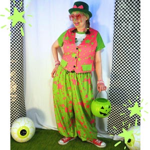 May include: A costume featuring a green top, a pink waistcoat with green stars, and matching green trousers with pink stars. The outfit includes a green top hat with a pink bow, heart-shaped glasses, beaded bracelets, and a green plastic jack-o'-lantern bucket.