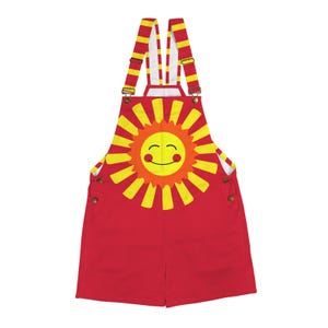 Puede incluir: Pantalones cortos con tirantes rojos con un gráfico de sol sonriente amarillo y naranja. Las correas son de rayas amarillas y rojas. Los pantalones cortos con tirantes tienen dos botones laterales.