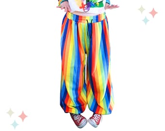 May include: Loose-fitting pants featuring a vibrant vertical rainbow stripe pattern in red, orange, yellow, green, blue, and purple. The pants have an elasticized waistband with a black drawstring cord and a relaxed, wide-leg silhouette.