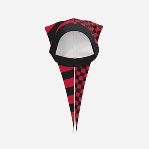 May include: A head covering featuring a split design with red and black horizontal stripes on one side and a red and black checkerboard pattern on the other. The item has a rounded crown, a black trim, and two long, pointed fabric tails hanging down.