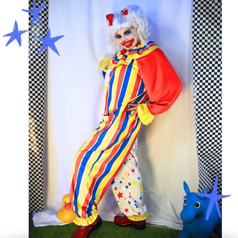 Op de afbeelding: Een clownskostuum bestaande uit een jumpsuit met lange mouwen met verticale rode, gele en blauwe strepen op het lijfje en &eacute;&eacute;n broekspijp, terwijl de andere broekspijp een witte stof heeft met een patroon van kleine rode en gele sterren.
