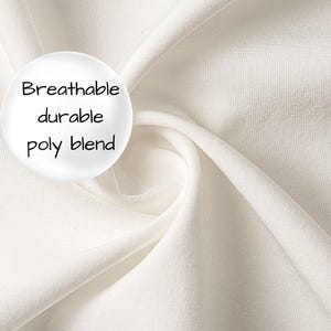 Op de afbeelding: Een effen gebroken witte stof met een gladde, geweven textuur en zachte plooien. Aan de linkerkant bevindt zich een cirkelvormige witte grafische overlay met de zwarte tekst: Breathable durable poly blend. Het materiaal oogt ondoorzichtig en egaal.