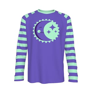 May include: A long-sleeved purple shirt with mint green striped sleeves. The front features a smiling crescent moon and stars design within a sunburst shape. The shirt has a round neckline and is likely made of a soft, comfortable material.