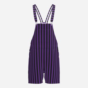 Puede incluir: Peto corto con un patrón de rayas verticales en colores alternos morado y negro. La prenda incluye tirantes ajustables con hebillas metálicas, un bolsillo frontal en el peto y dos bolsillos laterales, terminando en perneras cortas.