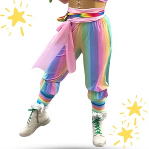 Könnte beinhalten: Regenbogenfarbene gestreifte Hose mit einer hellrosa Taillenschärpe, kombiniert mit passenden regenbogenfarbenen Leggings und weißen Schnürstiefeln mit grünen Schnürsenkeln. Das Design umfasst ein hellrosa Korsett-Oberteil mit weißer Schnürung.