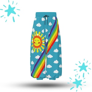 Puede incluir: Pantalones de chándal azules con un patrón repetitivo de nubes blancas, un gráfico grande de un sol amarillo sonriente en la pierna izquierda y una franja diagonal de arcoíris en el frente. Tienen cintura elástica con cordones negros.