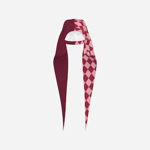 May include: A long-tailed head covering featuring a split design. One side is a solid deep burgundy color, while the other side displays a repeating diamond pattern in alternating shades of light pink and deep burgundy. The interior is white.