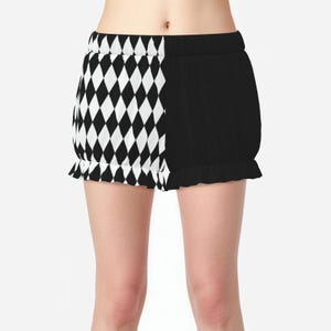 May include: Shorts featuring a split design with a black and white diamond harlequin pattern on one side and solid black on the other. The shorts have an elasticized waistband and a ruffled hemline, providing a gathered, voluminous silhouette.