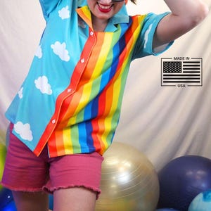 May include: A button-up shirt with a rainbow stripe design on the front and a light blue background with white cloud patterns. The shirt is paired with pink shorts. A "Made in USA" label is visible.