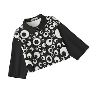 Puede incluir: Una camisa de botones recortada en blanco y negro con un patrón de círculos blancos con centros negros. La camisa tiene cuello y mangas cortas. El texto "ABYSS WARES" está impreso en el cuello.