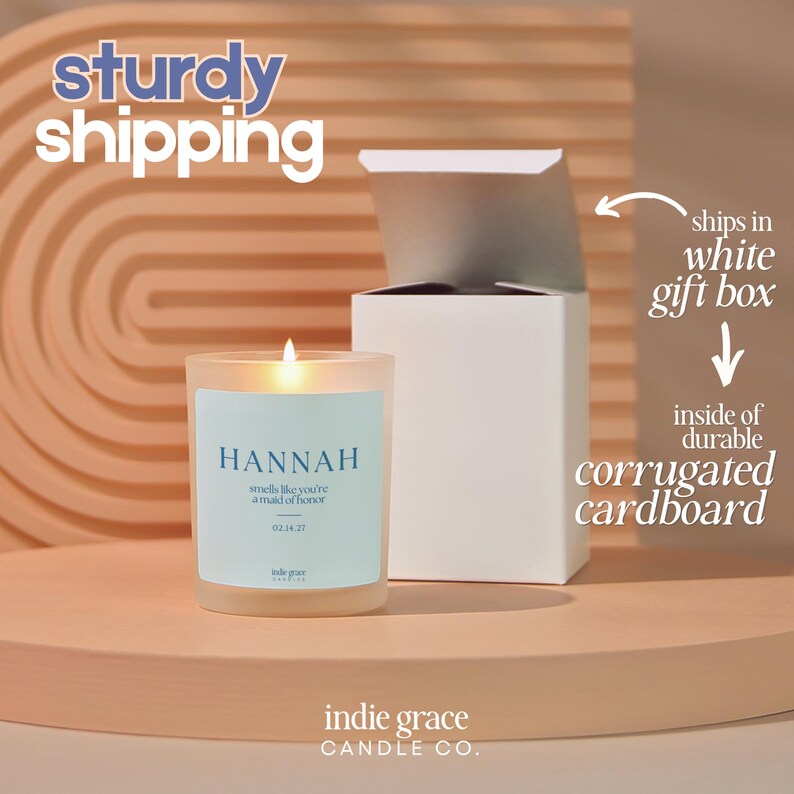 Pu&ograve; includere: Una candela accesa in un barattolo di vetro smerigliato con un'etichetta blu che recita "HANNAH smells like you're a maid of honor 02.14.37." La candela &egrave; appoggiata su una superficie di legno accanto a una scatola regalo bianca. Il testo "sturdy shipping" &egrave; in alto.