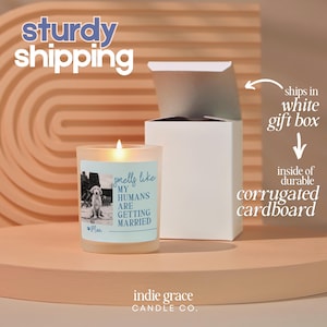 Op de afbeelding: Een brandende kaars in een matglazen pot met een etiket met de tekst "Smells like my humans are getting married". De kaars zit in een witte geschenkverpakking met golfkarton aan de binnenkant. De tekst "sturdy shipping" staat bovenaan.