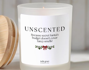 May include: A frosted glass candle with a wooden lid. The label reads: UNSCENTED Because secret Santa's budget doesn't cover fancy smells! with a small illustration of holly leaves and a red bow, and the text indie grace CANDLES at the bottom.