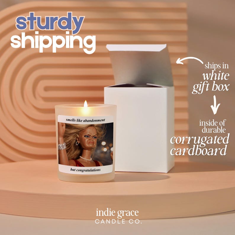 K&ouml;nnte beinhalten: Eine brennende Kerze in einem Milchglas mit einem Etikett mit der Aufschrift "smells like abandonment but congratulations". Die Kerze steht neben einer wei&szlig;en Geschenkbox. Der Text "sturdy shipping" steht oben.