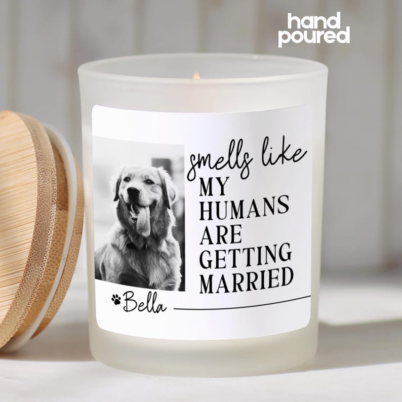 Op de afbeelding: Een matglazen kaars met een houten deksel. De kaars heeft een zwart-wit foto van een hond en de tekst "smells like MY HUMANS ARE GETTING MARRIED". De naam van de hond, "Bella", staat ook op het etiket.