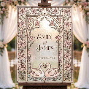 May include: A wedding sign with the names "Emily & James" and the date "October 12, 2024". The sign has a stained-glass design with pink flowers, green leaves, and two swans. It is displayed on a wooden easel, suitable for a wedding.