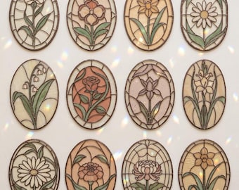 May include: A collection of twelve oval-shaped stained glass panels, each featuring a different floral design. The panels showcase various flowers in shades of white, pink, orange, and yellow, with green leaves and stems. The panels are framed with a dark brown border.