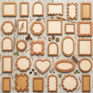 Op de afbeelding: Een verzameling houten frames in verschillende vormen en maten, waaronder vierkanten, rechthoeken, ovalen en een hart. De frames hebben een natuurlijke houtkleur met een donkerdere, decoratieve rand. Sommige frames zijn effen, terwijl andere geschulpte of sierlijke randen hebben. Gedroogde bloemen en kleine knopen zijn rond de frames verspreid.