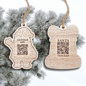 May include: Two wooden Christmas tree decorations. One is Santa-shaped, the other a gift bag. Both feature a maze design and a QR code. Text on the Santa ornament reads "scan to track santa." The gift bag ornament says "SANTA TRACKER."