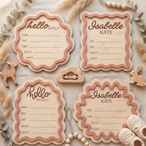 Puede incluir: Carteles de madera para anuncios de bebé con bordes festoneados en madera clara y rosa. Los carteles tienen espacio para escribir los datos del bebé. Las palabras "hello world" e "Isabelle KATE" están escritas en los carteles. Un ciervo, un conejo y una nube de madera también están en la imagen.