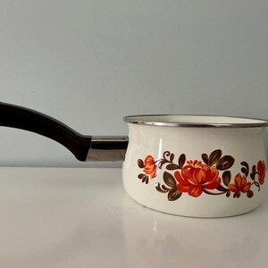 Puede incluir: Cacerola de esmalte blanco con mango negro y diseño floral con flores naranjas y marrones.