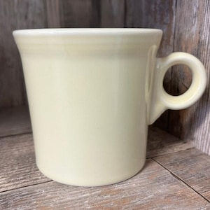 May include: A pale yellow ceramic mug with a rounded handle. The mug is sitting on a wooden surface.
