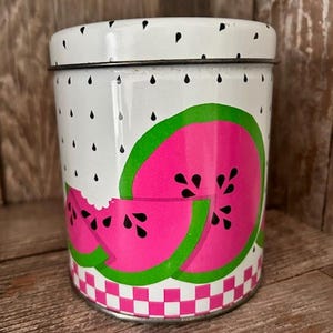 Puede incluir: Un tarro de metal blanco con un diseño de sandía rosa y verde. El tarro tiene un patrón de cuadros alrededor de la parte inferior.