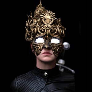 May include: A person wearing a gold, ornate mask with glowing white eyes. The mask has a detailed design with intricate patterns and a crown-like top.