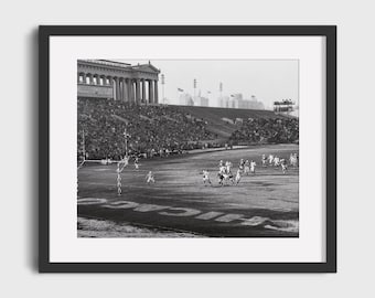 Könnte beinhalten: Ein Schwarzweißfoto eines Fußballspiels, das in einem Stadion gespielt wird. Das Stadion ist mit Zuschauern gefüllt und die Spieler rennen auf dem Spielfeld herum. Das Spiel findet vor einem großen Gebäude mit Säulen statt.