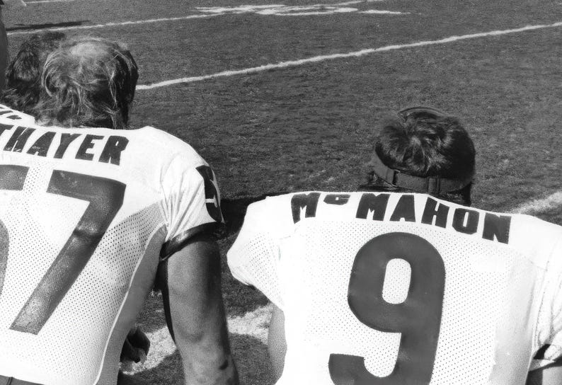 May include: Two football players in uniform, one with the name "THAYER" and the number "17" on their jersey, the other with the name "MC MAHON" and the number "9" on their jersey.