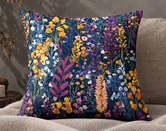 May include: A square throw cushion featuring a vibrant botanical print on a dark navy blue background. The design displays a dense arrangement of wildflowers in shades of golden yellow, bright orange, magenta, purple, and white, creating a colourful floral pattern.