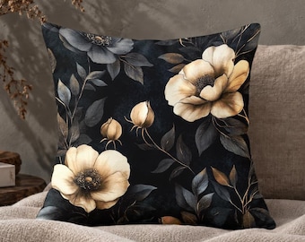 May include: A square throw pillow featuring a dark black background with a floral pattern of large, light beige, open-petaled flowers and closed buds, interspersed with dark grey and muted gold leaves and stems across the entire surface.