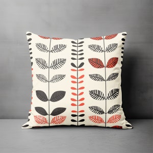May include: A white throw pillow with a black and red floral pattern. The pattern features stylized leaves and stems.
