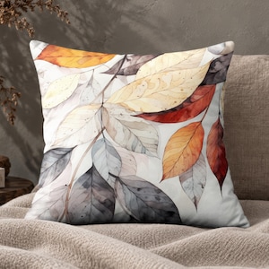 May include: A square throw pillow featuring a watercolor-style illustration of overlapping autumn leaves in shades of orange, red, yellow, and grey against a white background. The design displays detailed leaf veins and soft color gradients.