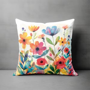 May include: A square decorative pillow featuring a watercolor floral design. The pillow showcases a vibrant array of flowers in shades of orange, red, pink, and blue, set against a white background. Green leaves and stems complete the design.