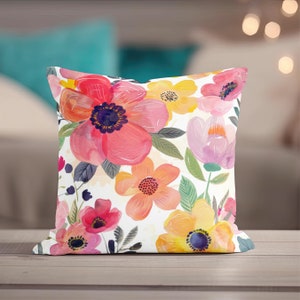 May include: A white pillow with a floral pattern. The flowers are pink, yellow, and orange and are painted in a watercolor style.